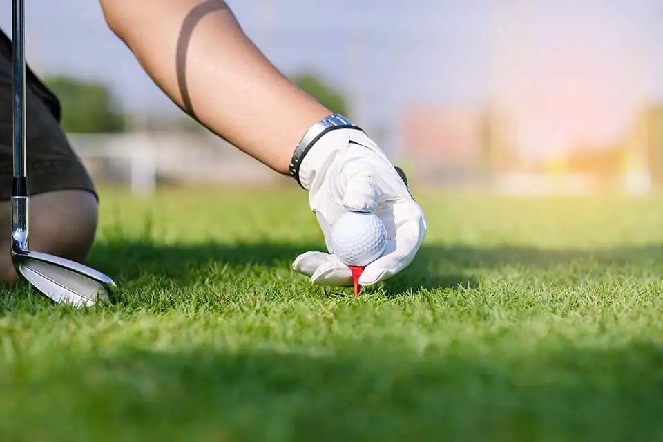 Hand in glove placing golf ball on tee in course